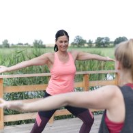 Zwei Frauen üben Yoga auf einer Terasse, die Ruhe und Entspannung in ihrer Sporttherapie fördert.